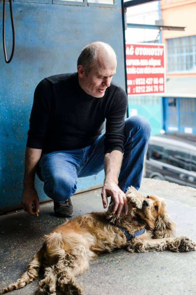 Man in spijkerbroek aait kriebelt buik van hond